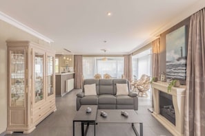 Een woonkamer met een grijze bank, een eethoek, een keuken en een open haard, inclusief een schilderij van een vuurtoren.