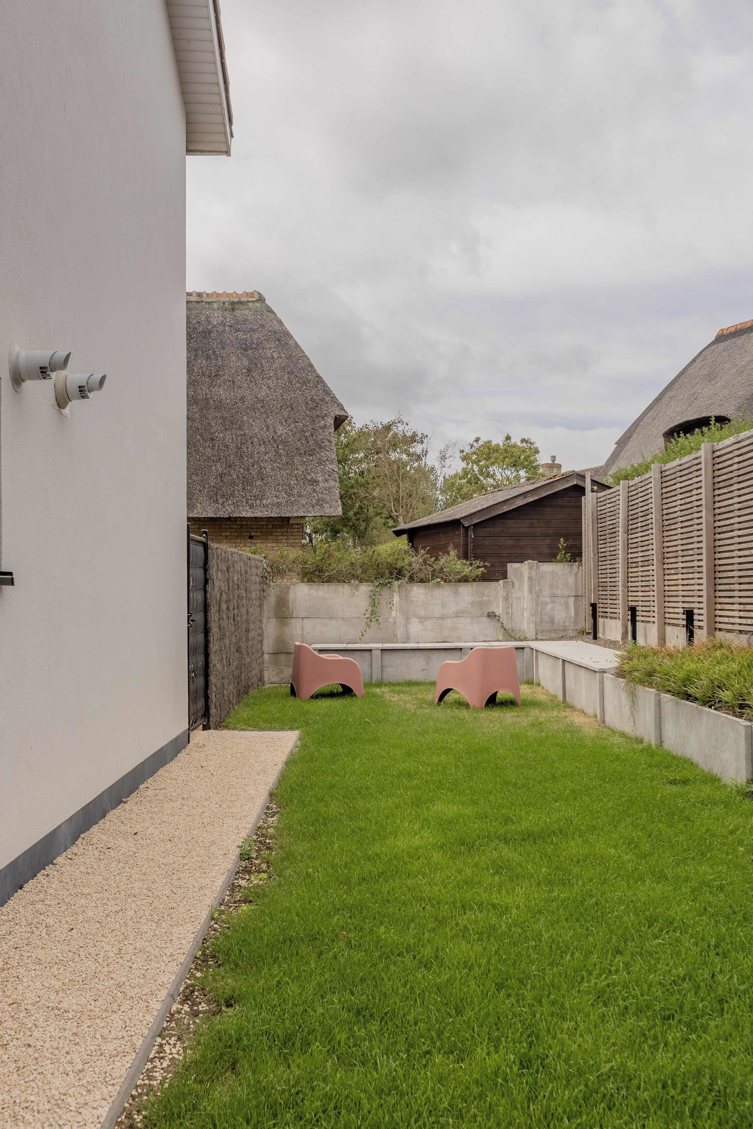 Een achtertuin met een verzorgd gazon, een betonnen pad en een houten omheining.