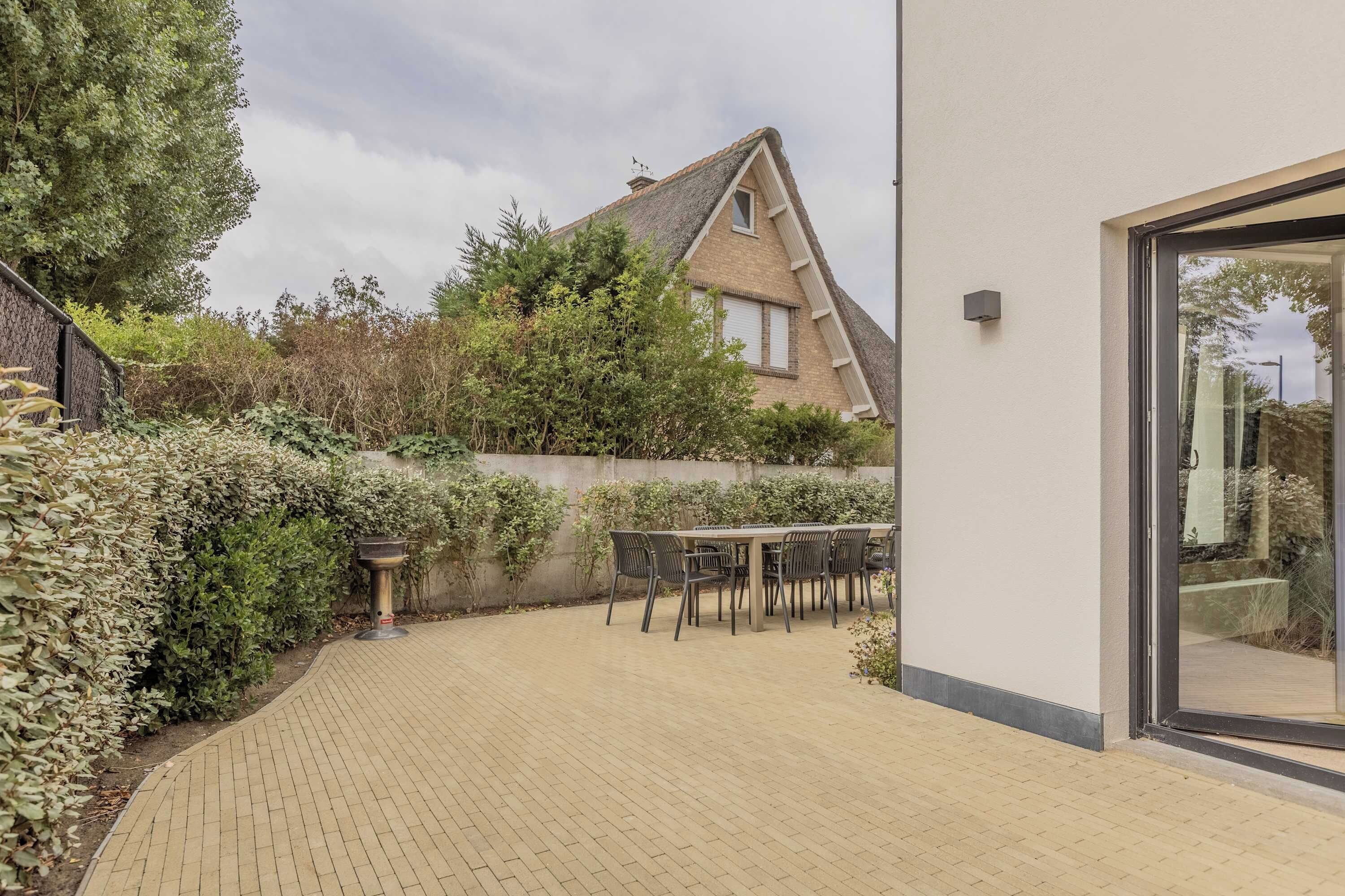 Une terrasse avec un sol en briques, une table entourée de chaises et une vue sur une maison dont le toit est en pente.