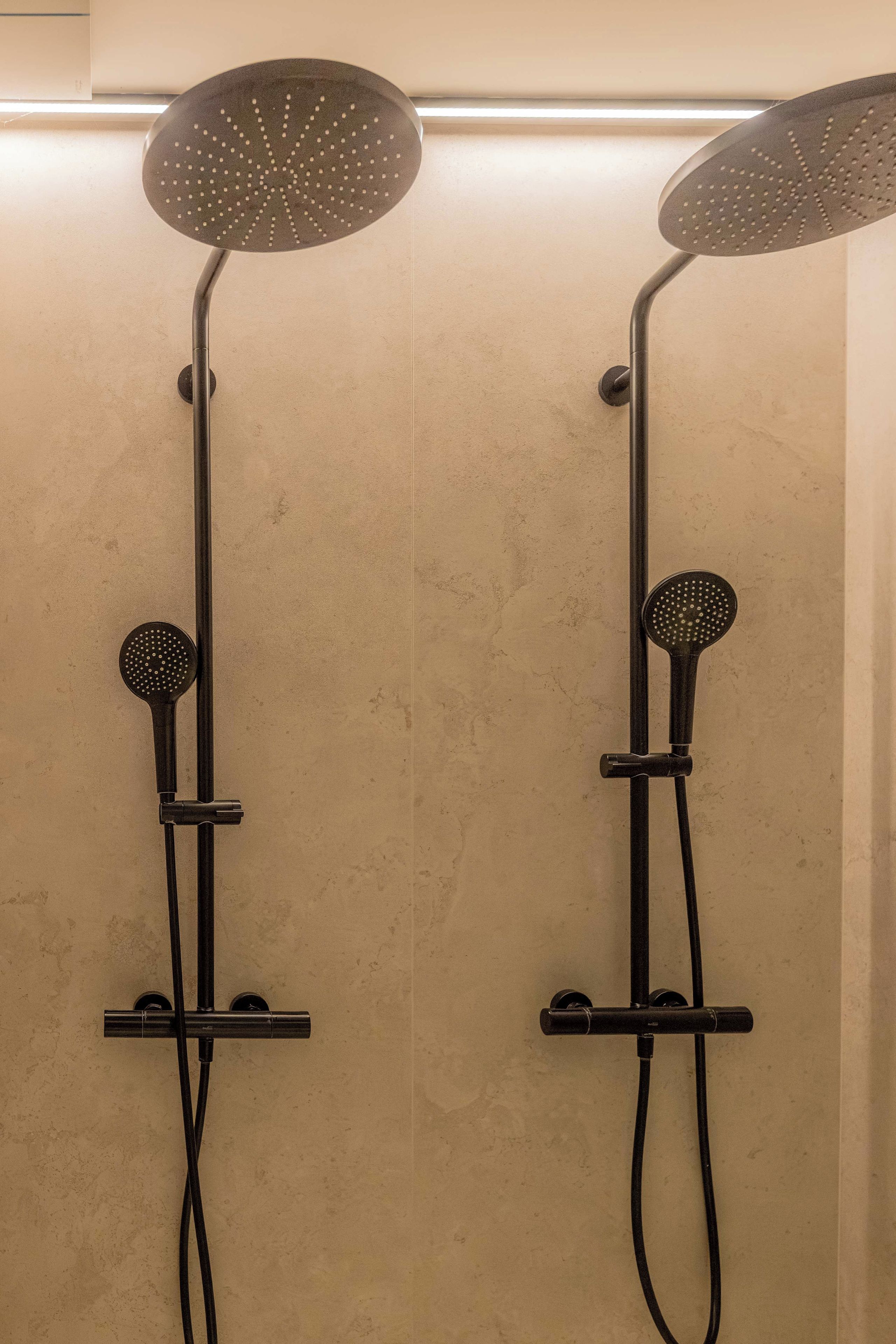 Deux pommeaux de douche fixés au mur, dotés d'une seule manette de commande, et installés sur un mur à texture.