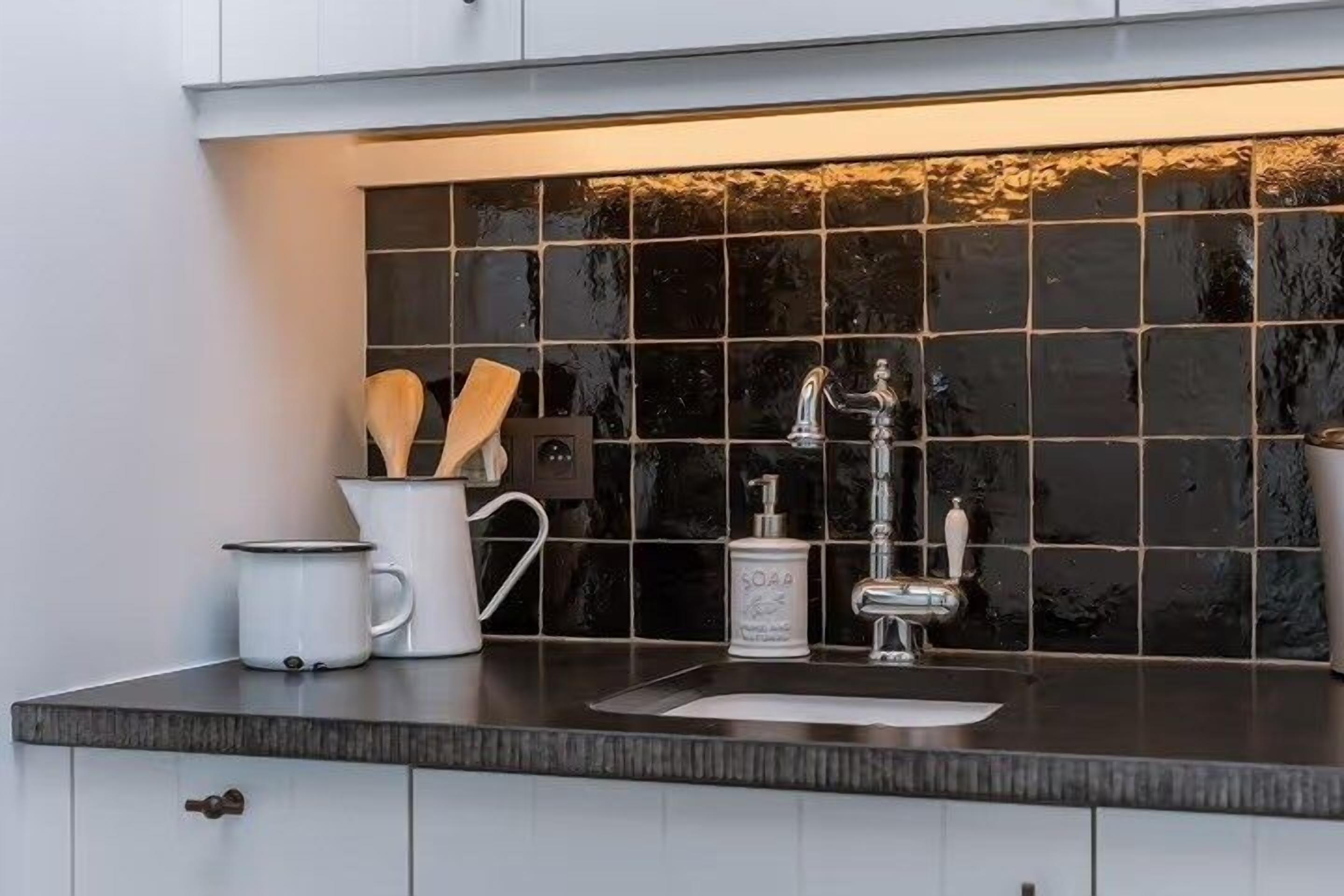 A kitchen with a black tiled backsplash, a stainless steel faucet, and a white countertop.
