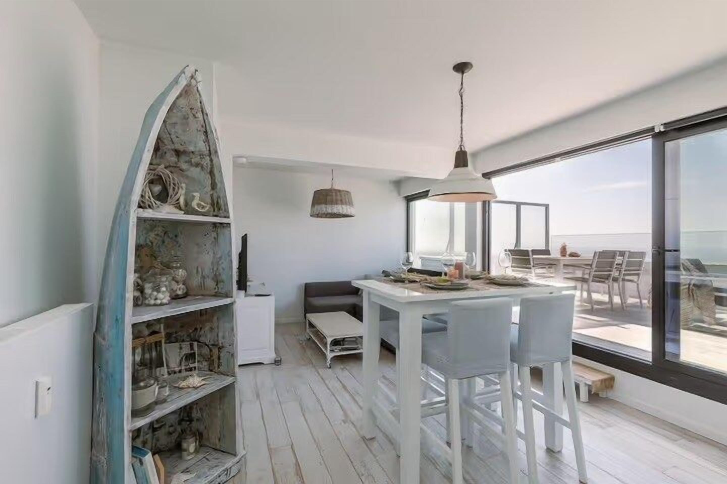 A modern interior with a dining area, a white shelf unit, and a large window overlooking a balcony.