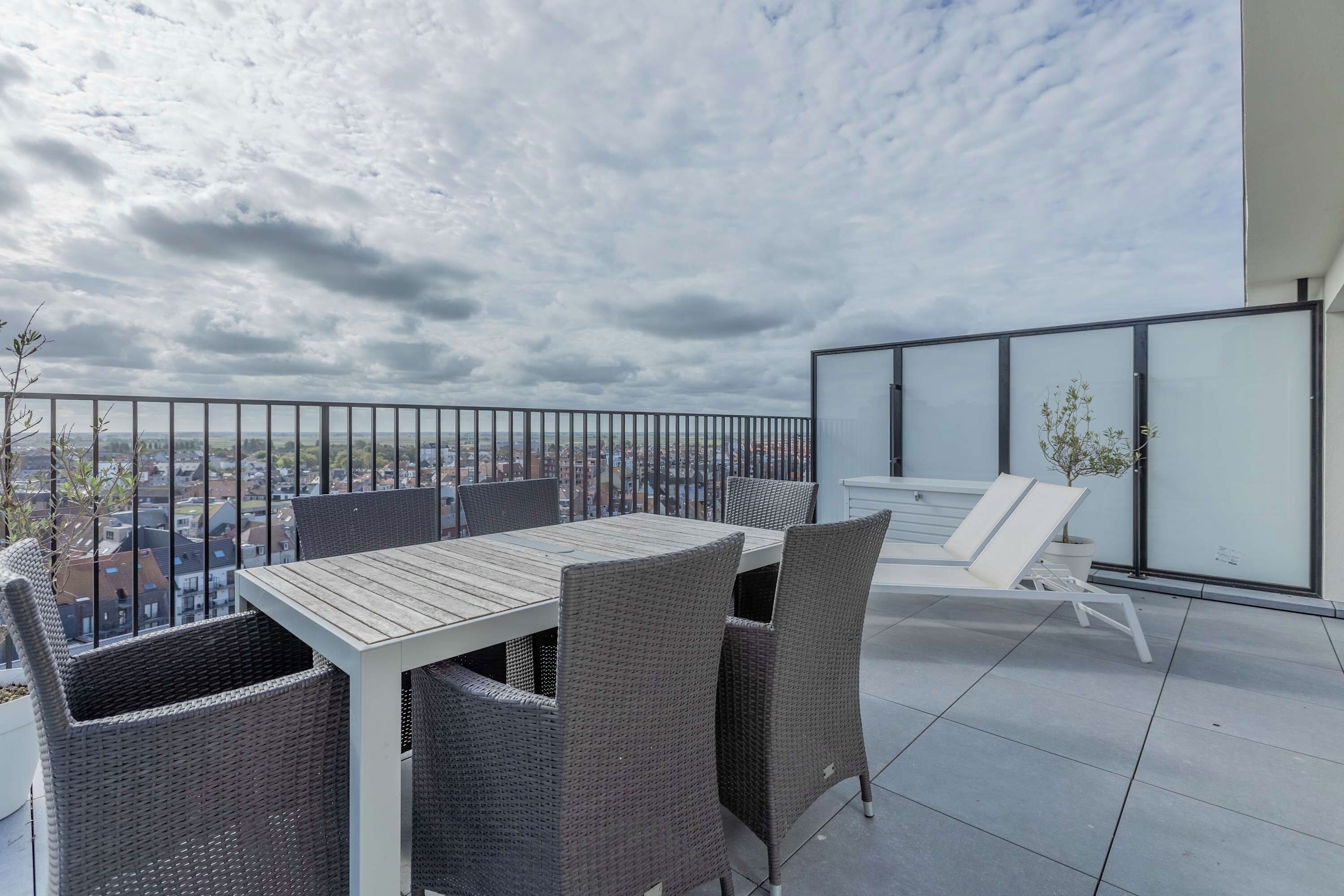 A balcony with a table and chairs, a glass railing, and a city view.
