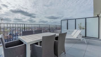 A balcony with a table and chairs, a glass railing, and a city view.