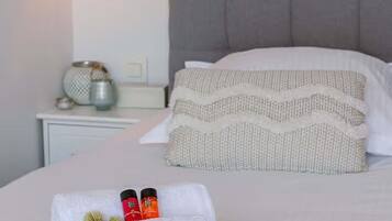 A neatly made bed with white linens, a grey headboard, and two pillows. There is a bedside table with a lamp and a decorative item.