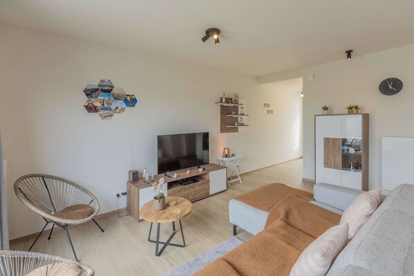 Un salon moderne avec un téléviseur à écran plat, un canapé, un fauteuil et une table basse.