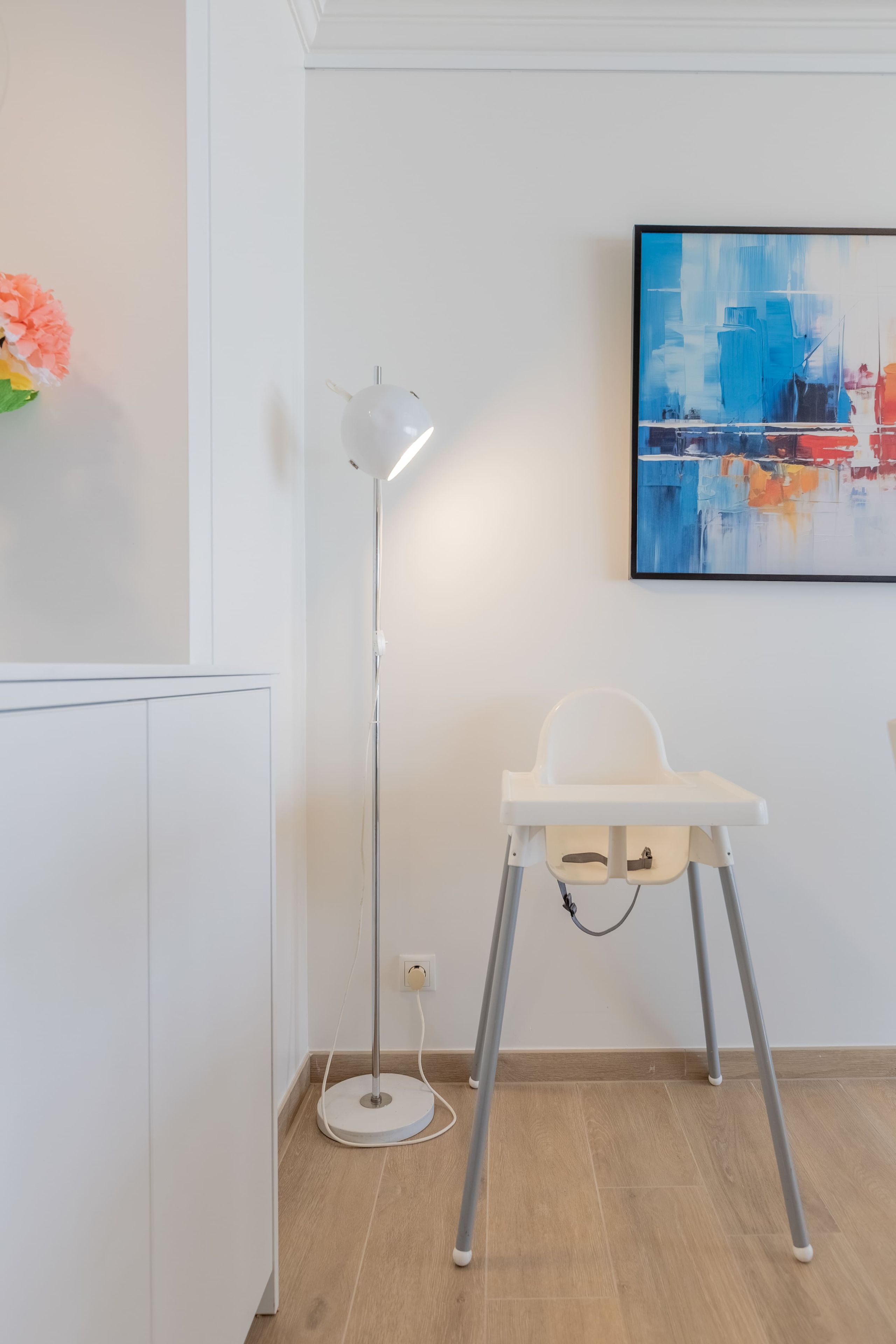 Una camera moderna con un lampadario da terra bianco, una sedia bianca e un quadro appeso al muro.