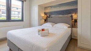 Una camera d'albergo con un letto grande, un quadro che raffigura una spiaggia e una finestra con vista sugli edifici.