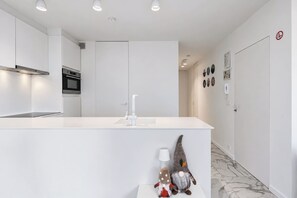Una cocina moderna con armarios blancos, horno empotrado y encimera blanca.