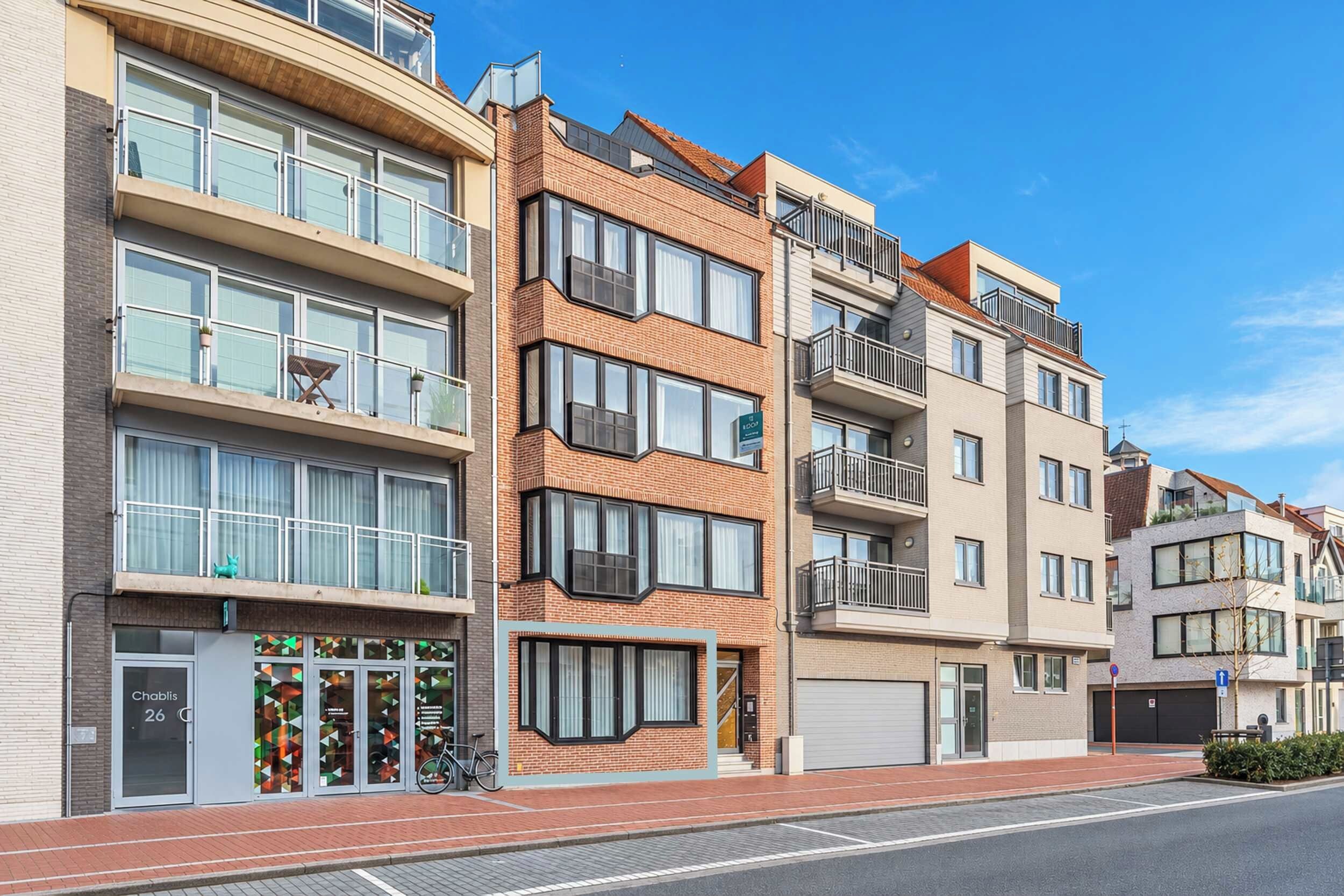 A multi-story residential building with balconies, large windows, and a ground-level entrance.