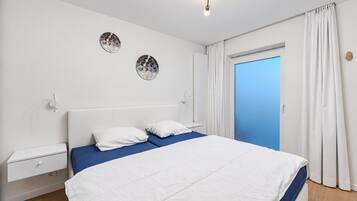 A bedroom with a bed, a nightstand, a wall-mounted light fixture, and a door with curtains.
