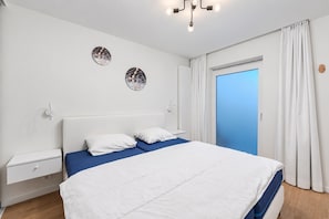 Un dormitorio con una cama, una mesita de noche, una lámpara de pared y una puerta con cortinas.