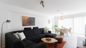 Un salon moderne comprenant un canapé d’angle, une table basse et un coin repas avec des chaises et une table.