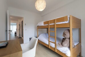 Un lit superposé avec un ours en peluche sur le lit du bas, un bureau avec une chaise et un luminaire suspendu.