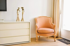 Ein Zimmer mit Holzboden, einem cremefarbenen Schrank mit zwei goldenen Statuen, einem Vintage-Orangensessel und einer Fußmatte mit dem Schriftzug 'HOME'.