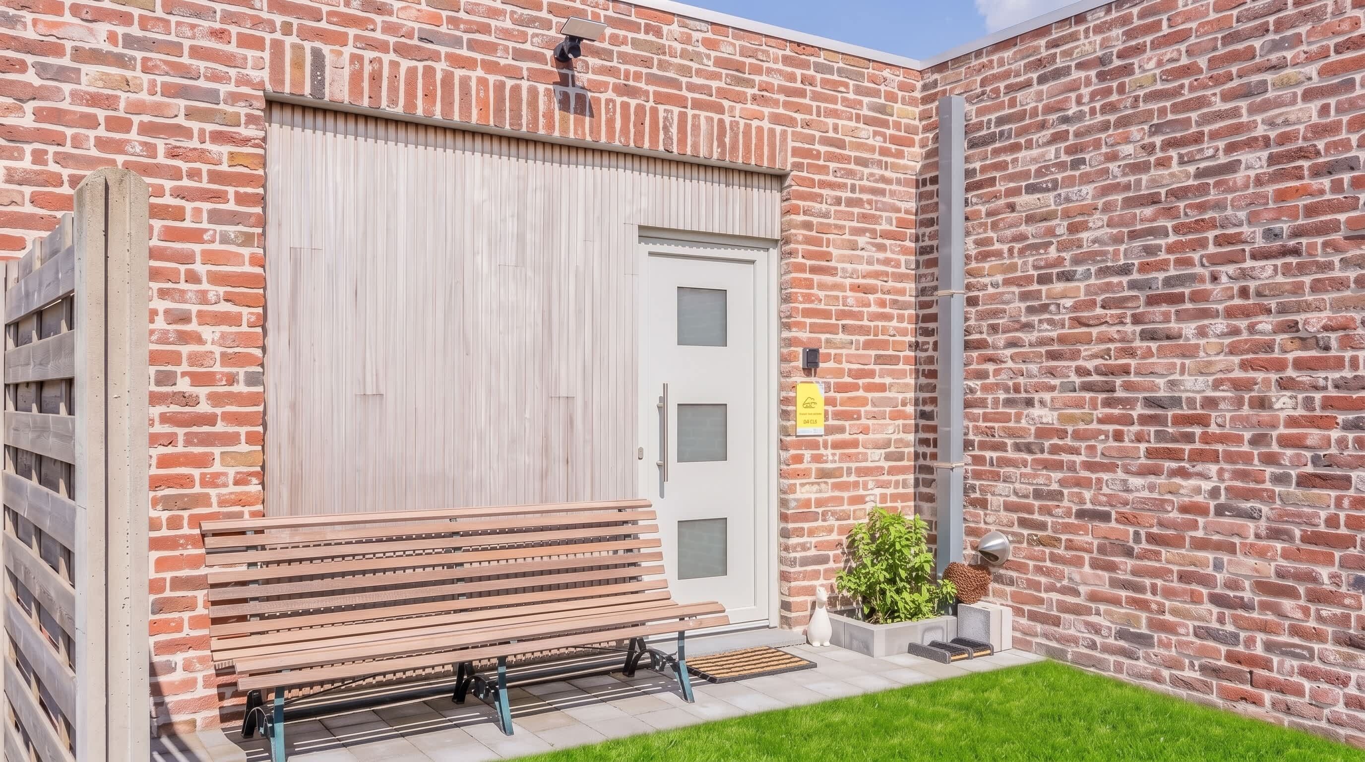 A brick building with a large garage door, a bench outside, and a small garden area.