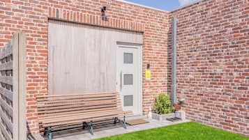 A brick building with a large garage door, a bench outside, and a small garden area.