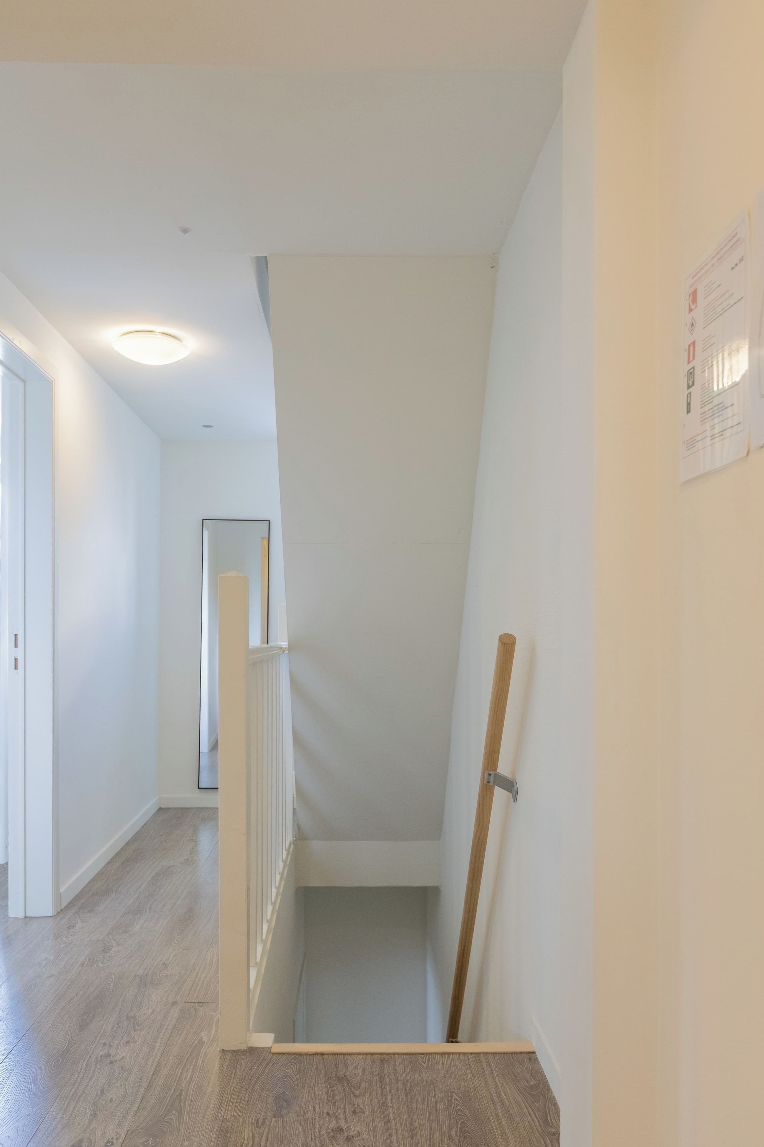 Ein helles, modernes Interieur mit Holzboden, weißen Wänden und einer Treppe, die in eine obere Ebene führt.