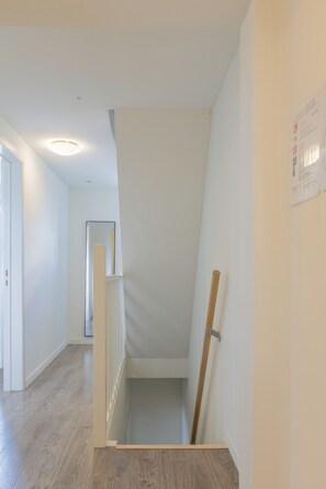 Een schoon, modern interieur met een houten vloer, witte wanden en een trap naar een hoger niveau.