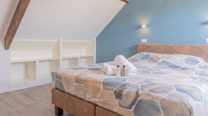 Ein Schlafzimmer mit geneigter Decke, einem Bett mit gemustertem Überwurf, einem Kopfteil und einer Wandleuchte.