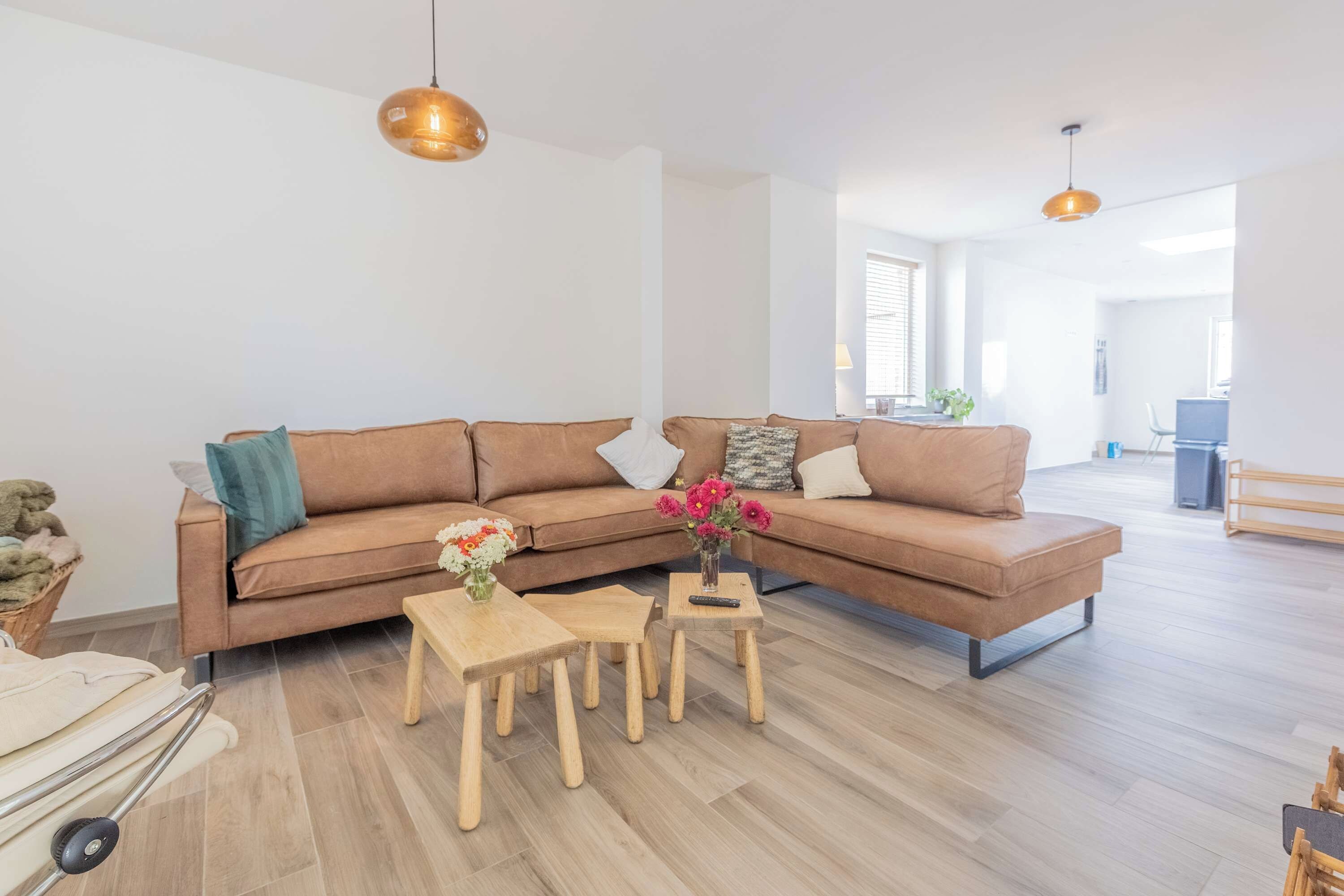 Ein stilvolles Wohnzimmer mit einem braunen Sofa, zwei Holztischen und einer Blumenvase.