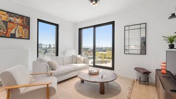 Ein modernes Wohnzimmer mit Sofa, Sessel, Couchtisch und großen Fenstern mit Blick auf die Stadt.