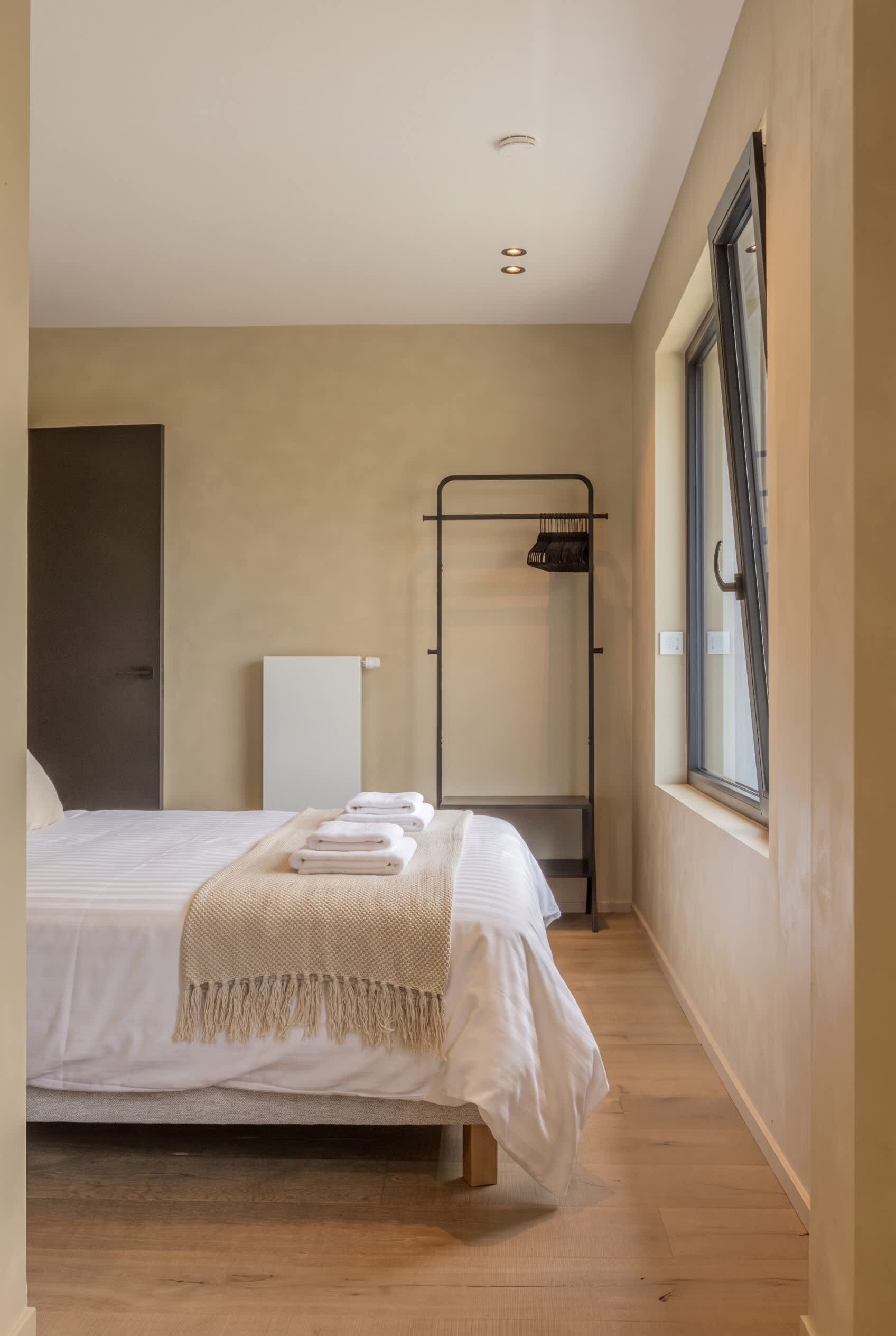 Ein Schlafzimmer mit Bett, Heizkörper, Fenster und einer Kleiderstange.
