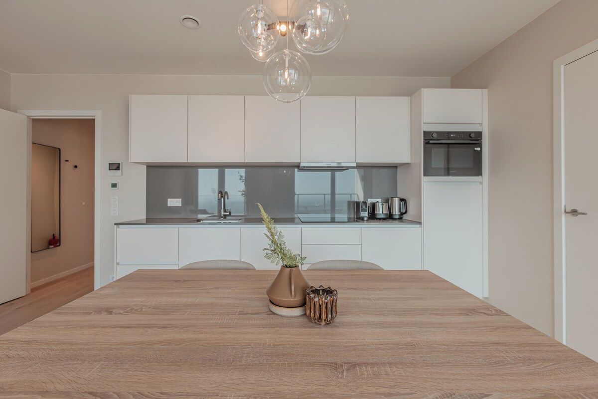 A modern kitchen with white cabinetry, a wooden dining table, and a pendant light.