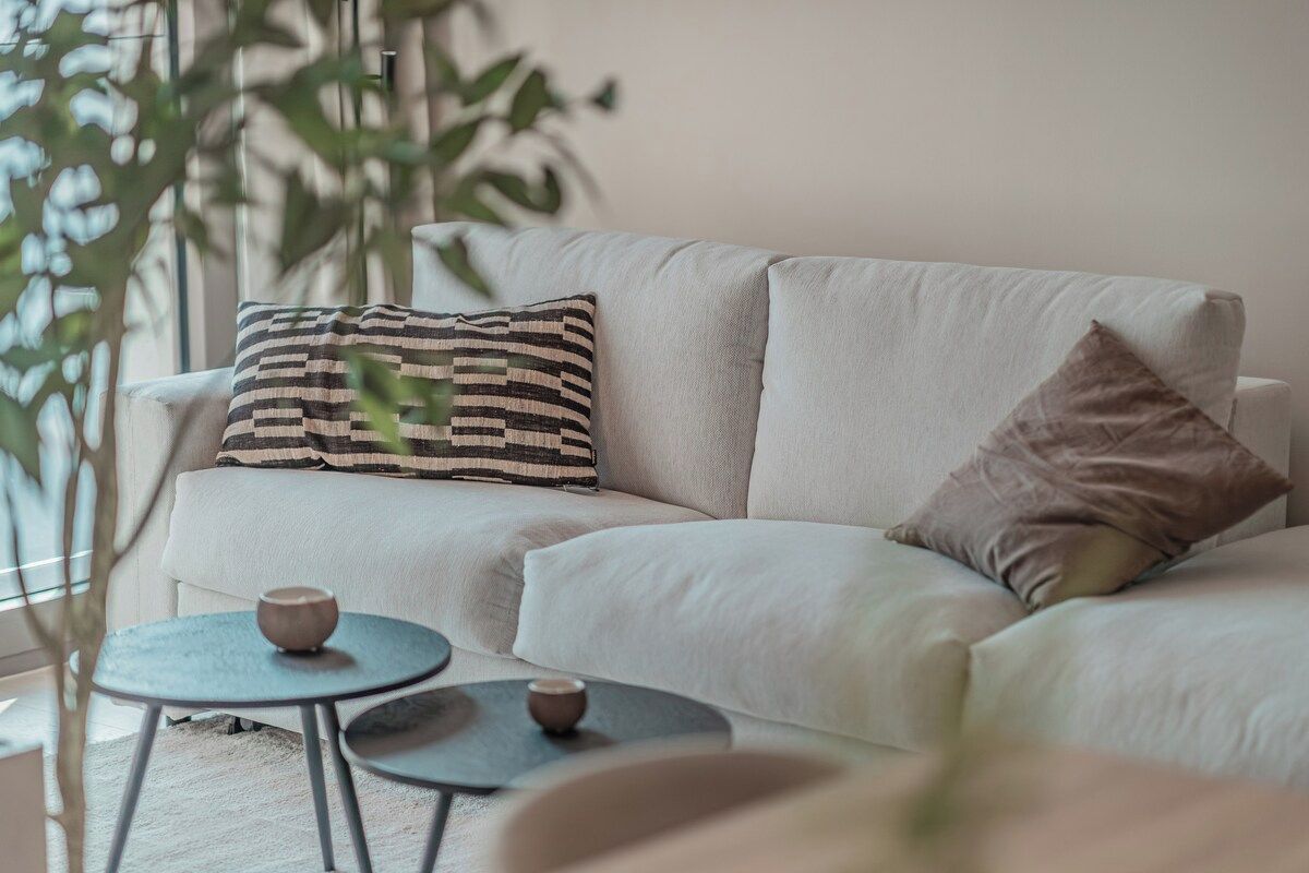 A modern living room with a sofa, two small round tables, and a patterned throw pillow.