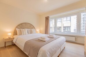 A hotel room with a large bed, a nightstand, a window with curtains, and a view of buildings outside. - Marée de la mer · 1 minute from the beach (Ostend)