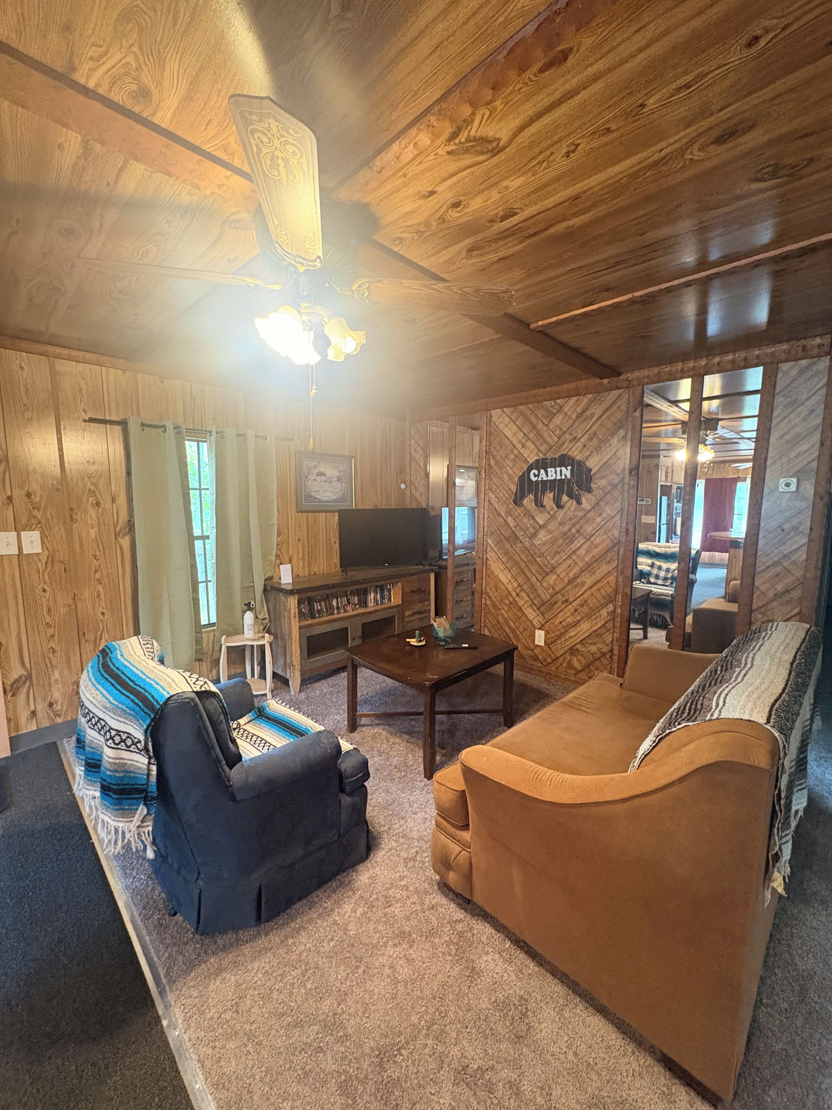 A cozy living room with wooden walls, a sofa, a couch, a TV, and a fireplace.