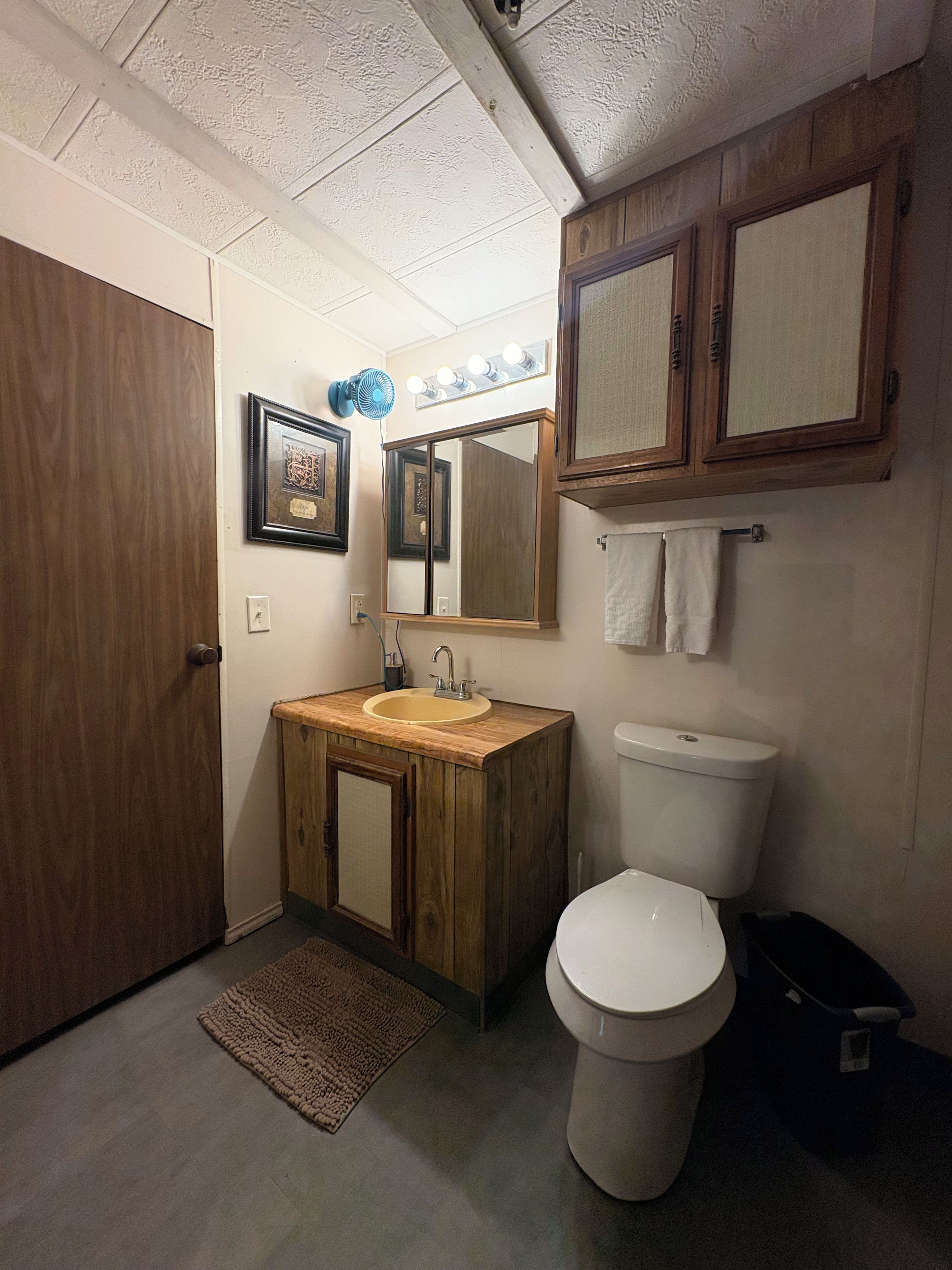 Un baño con tocador de madera, lavamanos, inodoro, espejo y toallero.