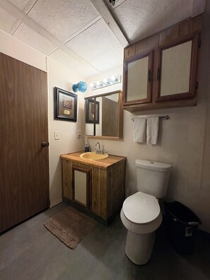 Un baño con tocador de madera, lavamanos, inodoro, espejo y toallero.