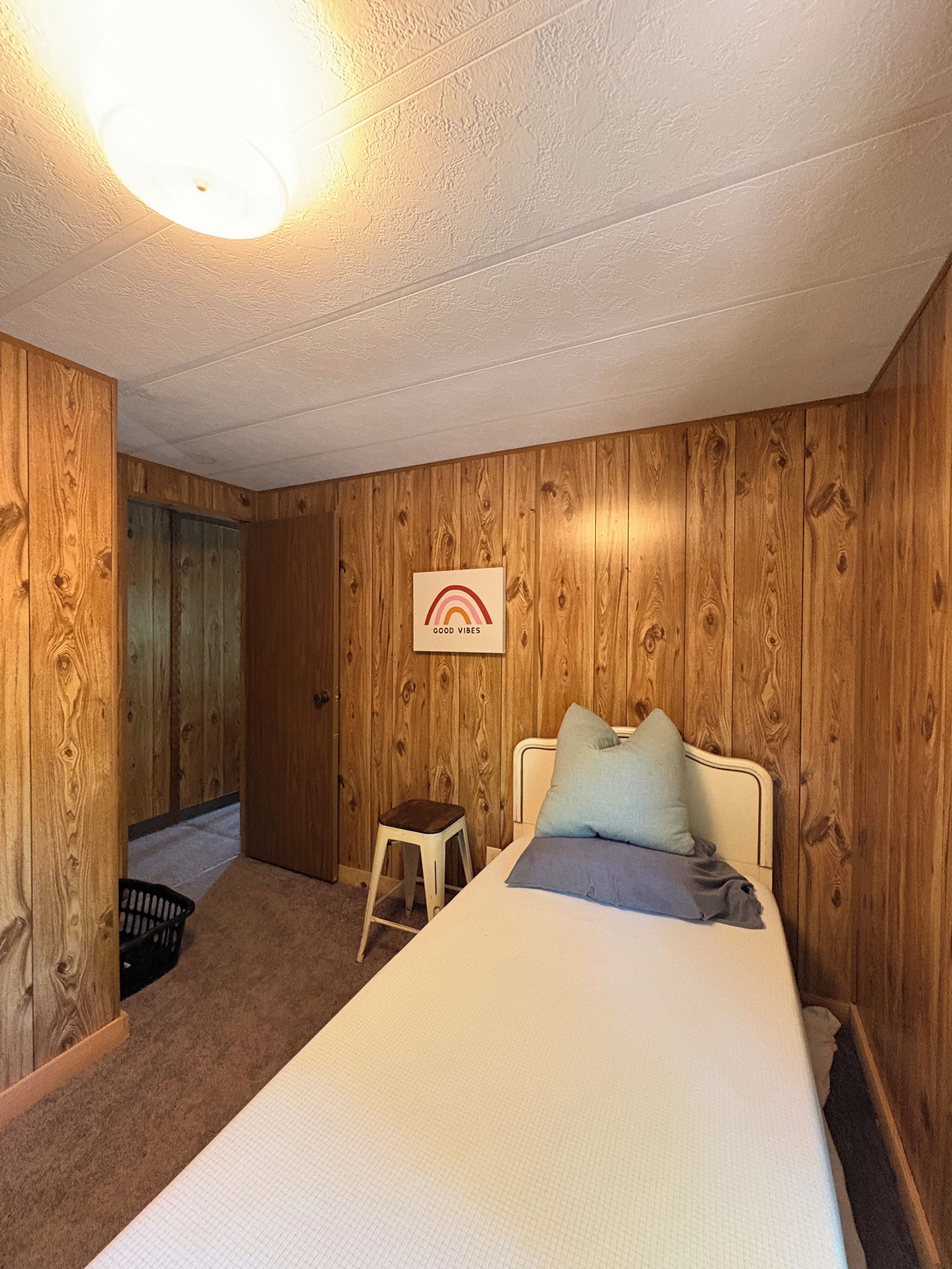 Un dormitorio con cama, mesita de noche, silla e imagen colgada en la pared.