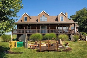 A two-story house with a deck, a chimney, and a fenced yard with a play area.