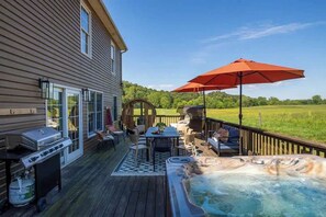 A deck with a hot tub, outdoor furniture, and a grill.
