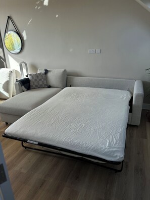 A modern living room with a sofa, a convertible bed, and a small table. - Bright skylit flat, sleeps 4, Nr Central line, with parking (Greenford)