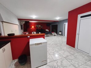 Cocina compacta con refrigerador, lavamanos y comedor con mesa y sillas.