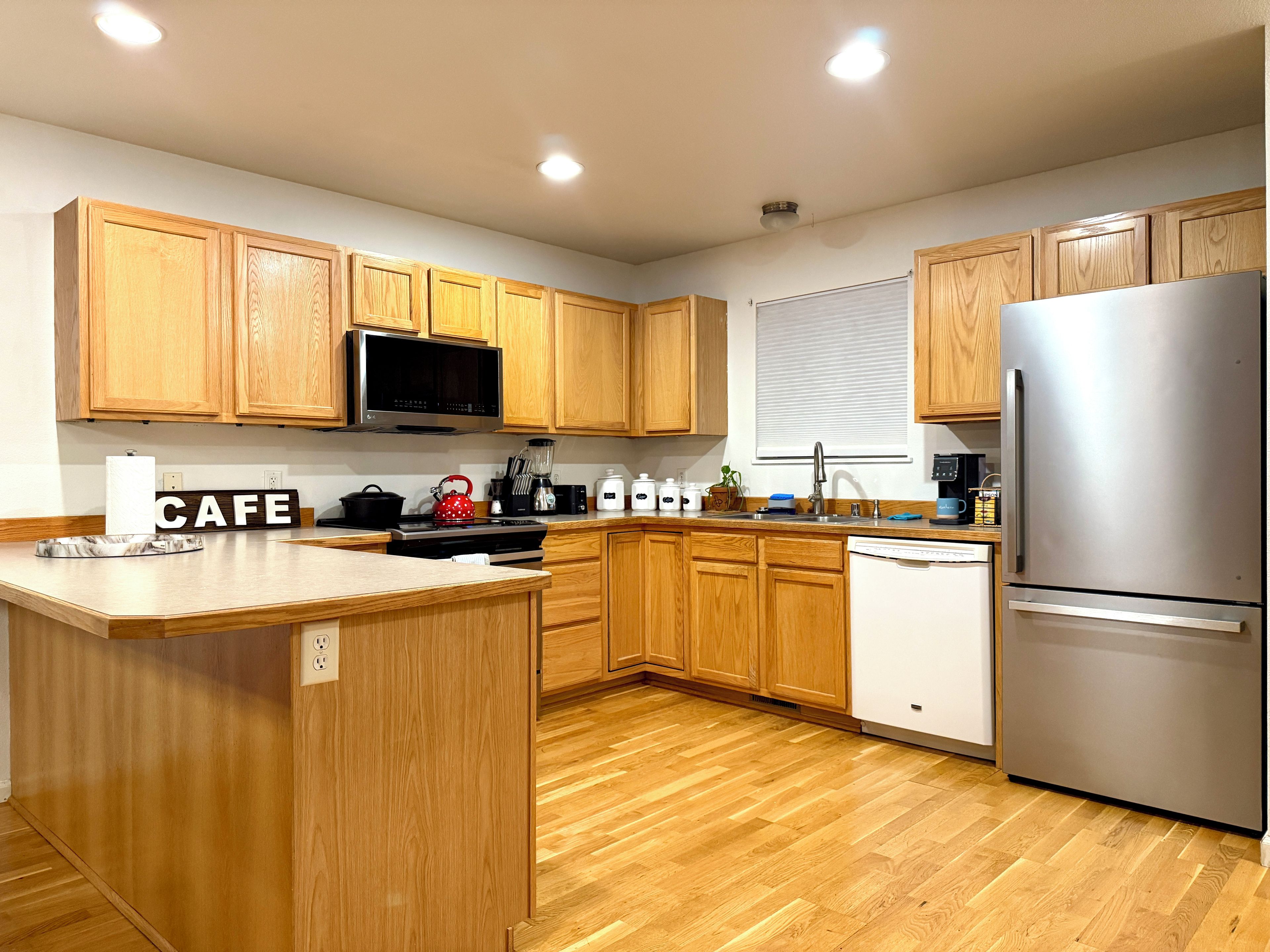 Una cocina moderna con armarios de madera, un refrigerador de acero inoxidable y una isla central con un letrero que dice 'CAFE'.