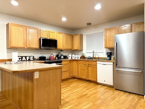 Una cocina moderna con armarios de madera, un refrigerador de acero inoxidable y una isla central con un letrero que dice 'CAFE'.