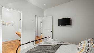 Un dormitorio con cama, televisor montado en la pared y baño visible a través de una puerta abierta.