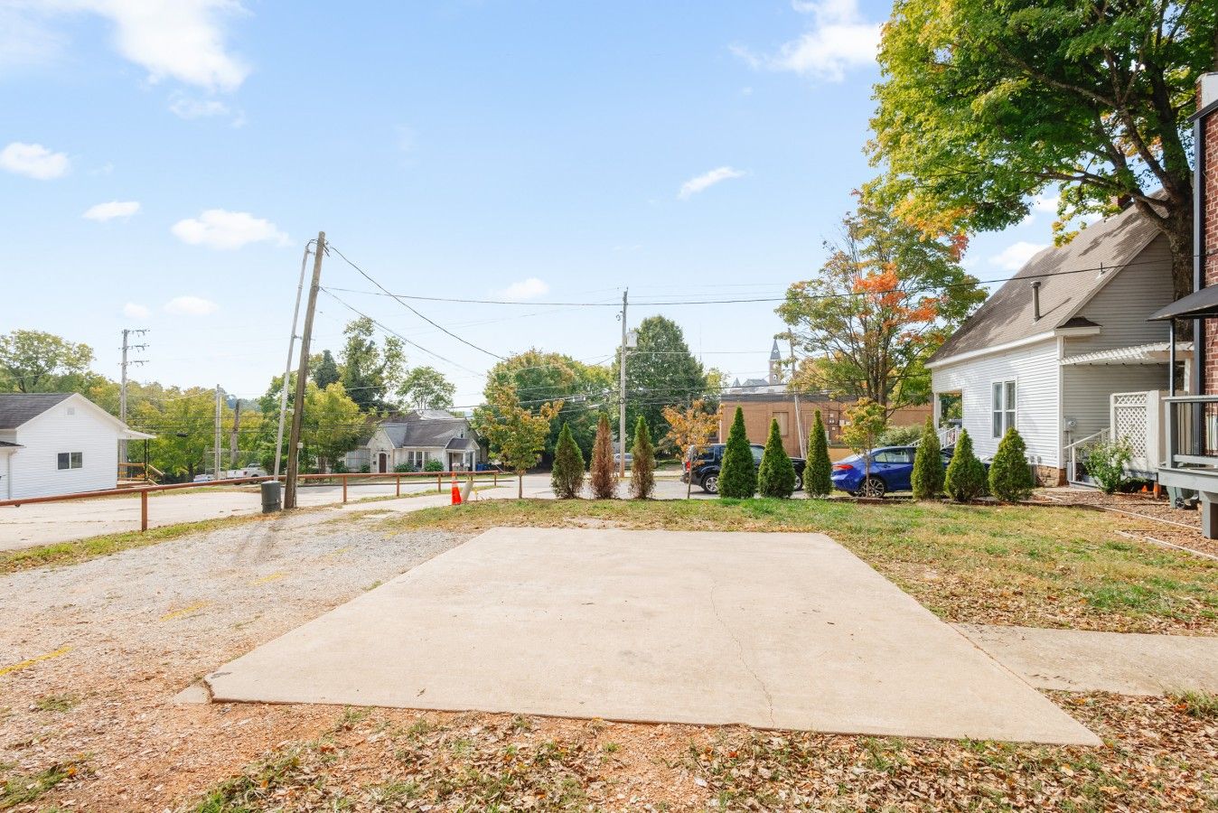 Un barrio residencial con entrada pavimentada, una casa con porche y un patio cercado.