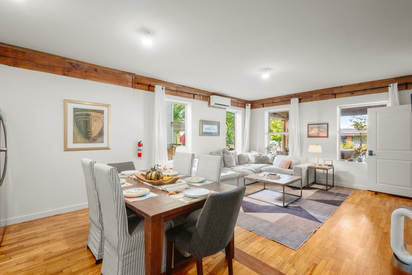 A spacious living room with a dining area, wooden beams on the ceiling, and large windows.