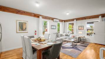 A spacious living room with a dining area, wooden beams on the ceiling, and large windows.