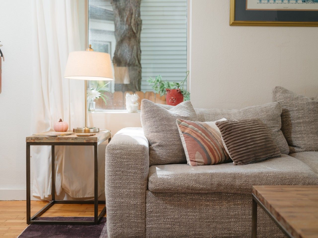 A living room with a sofa, a small table with a lamp, and a framed picture on the wall.