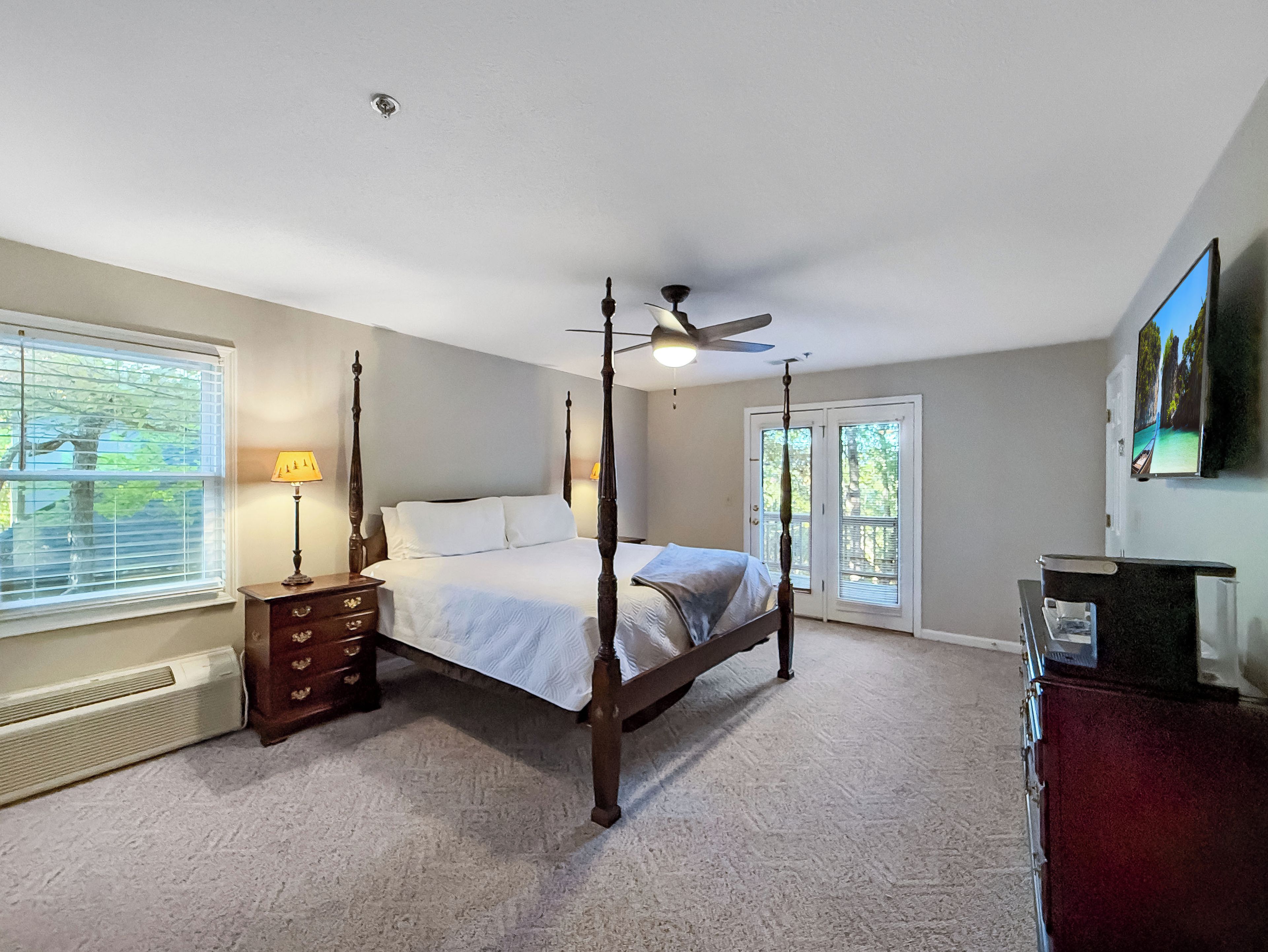 A four-poster bed with a ceiling fan, a dresser with drawers, a radiator, and a painting on the wall.