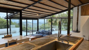 A modern interior with a large window, a dining area, and a seating area with a view of the outdoors. - Arabian Horse Farm House · Ocean View · Monteverde · Adults Only (Monteverde)