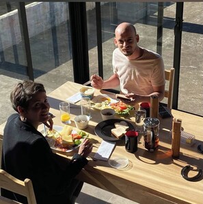 Twee personen dineren aan een tafel met uitzicht door grote ramen.