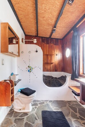 Een badkamer met een stenen vloer, een witte badkuip, een houten wastafelmeubel en een spiegel.
