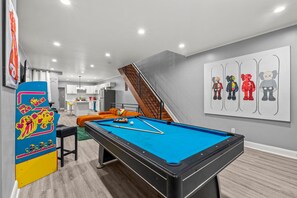 A modern living room with a pool table, a sofa, and a staircase leading to an upper level. - HYPE BEAST THEMED STR (Philadelphia)